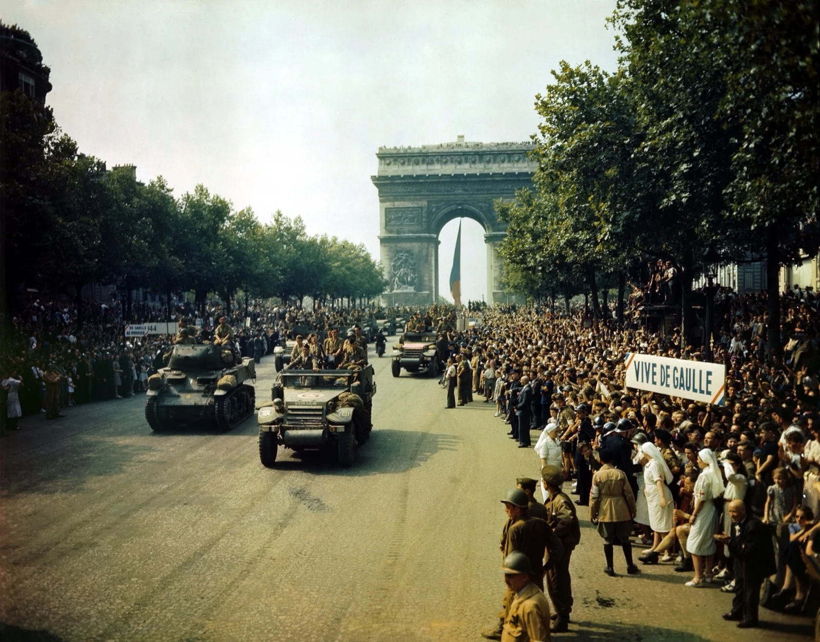 Foule immense massée sur les Champs-Élysées lors du défilé de la Libération, véhicules blindés de la 2e DB de Leclerc passant devant l'Arc de Triomphe, banderole « Vive de Gaulle », 26 août 1944.