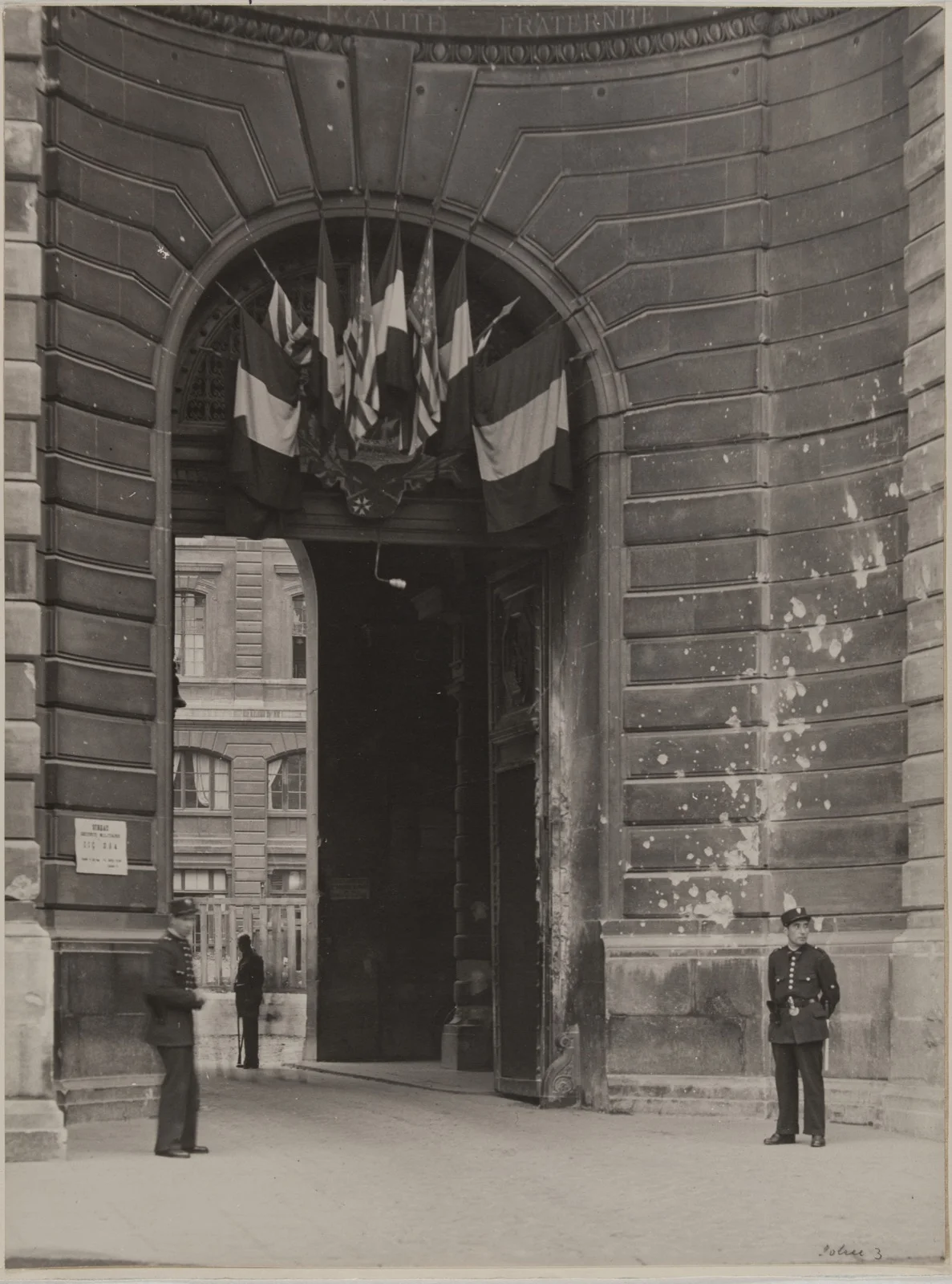 Portail de la Préfecture de Police de Paris orné de drapeaux alliés et tricolores, avec impacts de balles sur la façade, août 1944