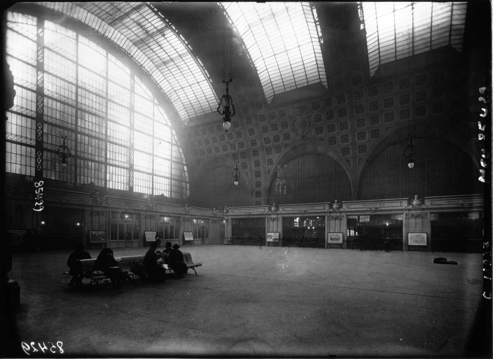 Hall de la gare d'Orsay à Paris, vers 1920 — grande verrière voûtée, voyageurs assis sur des bancs dans la lumière tamisée